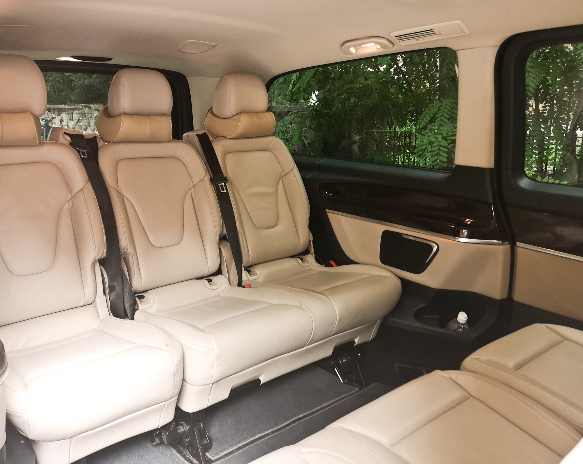 Wnętrze luksusowego busa z beżowymi skórzanymi fotelami, widok z tyłu kabiny pasażerskiej, butelka wody w uchwycie.