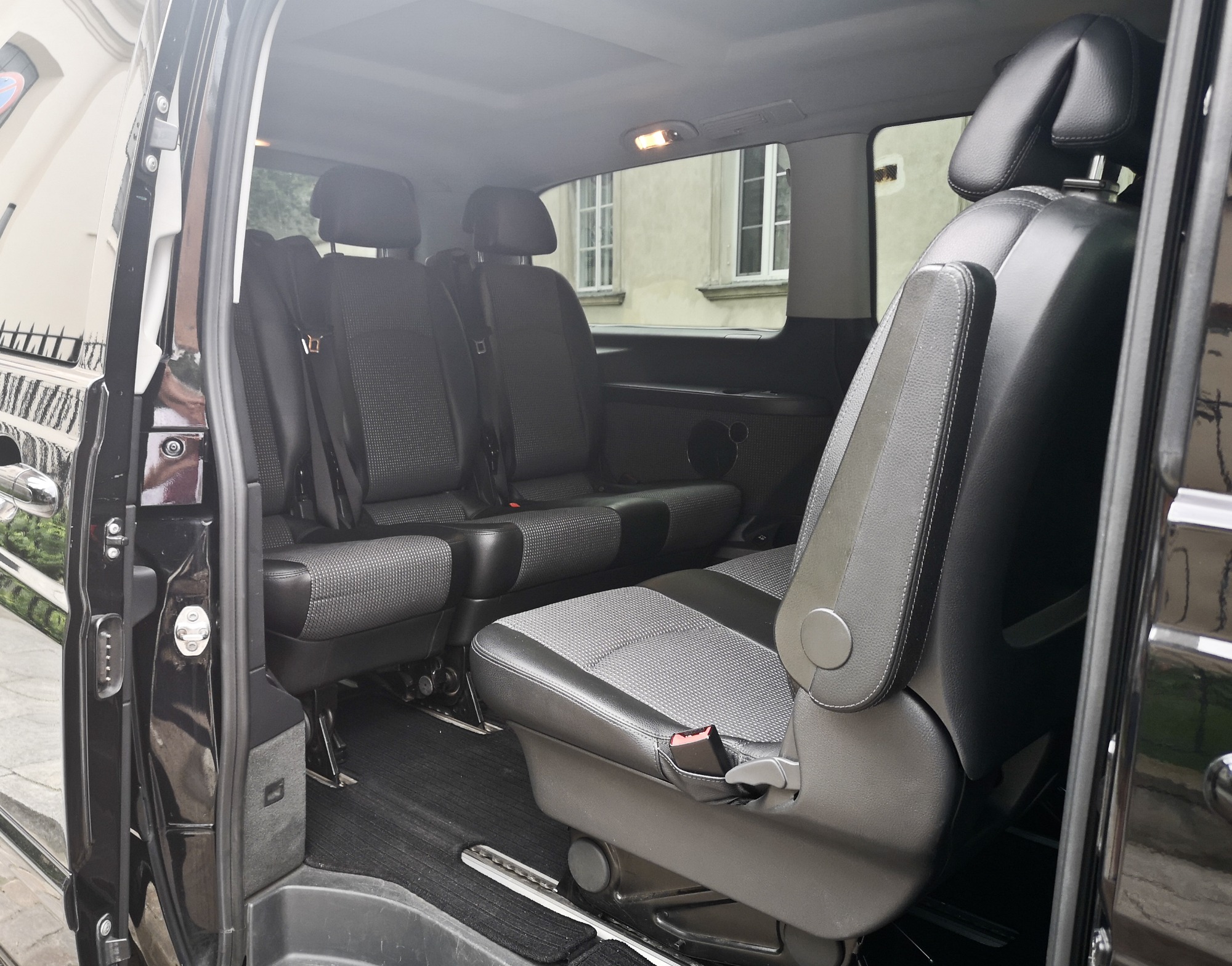 Wnętrze czarnego vana z jasnoszarymi fotelami w kratkę, widok z otwartych drzwi bocznych na trzy rzędy siedzeń.