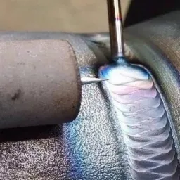 Precyzyjne łączenie metalowych elementów rur, widoczne tęczowe przebarwienia na spoinie świadczące o wysokiej temperaturze i jakości wykonania.