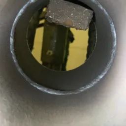 Wnętrze metalowej rury z fragmentem metalu przyspawanym w środku; widoczne ślady obróbki i niedoskonałości spoiny.