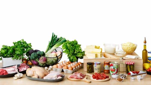 Bogaty wybór świeżych produktów spożywczych, w tym warzywa, owoce, mięso, nabiał i przyprawy, ułożonych na blacie w jasnym świetle, z przewagą białego tła.