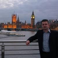 Mężczyzna w marynarce oparty o barierkę na tle Big Bena i Houses of Parliament w Londynie, widok na Tamizę.