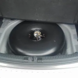 Toroidalny zbiornik na gaz LPG zamontowany w bagażniku samochodu osobowego, widoczny od góry, obok butelka płynu chłodniczego.