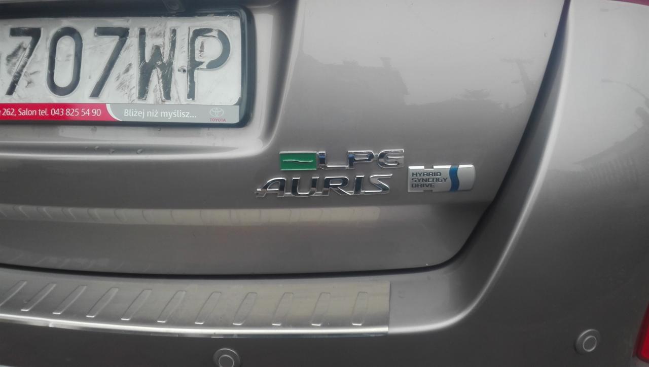 Tył samochodu Toyota Auris Hybrid z naklejką LPG, widoczna tablica rejestracyjna i emblematy.