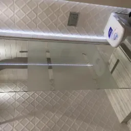 Nowoczesna kabina prysznicowa z deszczownicą i częściowo matową szybą, białe płytki z geometrycznym wzorem na ścianach, podświetlenie LED nad kabiną i wisząca toaleta z boku.