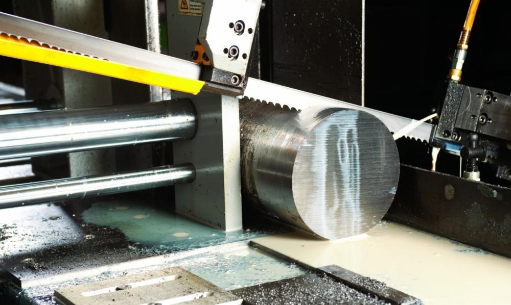Automatyczna piła taśmowa przecina gruby, okrągły pręt metalowy chłodzony cieczą.