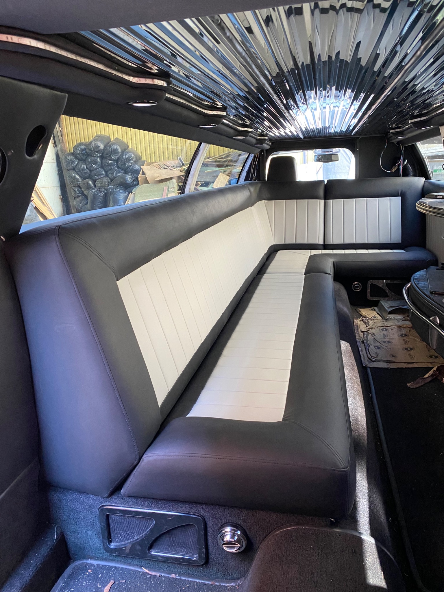 Wnętrze luksusowej limuzyny z odnowioną tapicerką w kolorze czarno-białym, z błyszczącym, lustrzanym sufitem i widocznymi elementami wykończeniowymi.