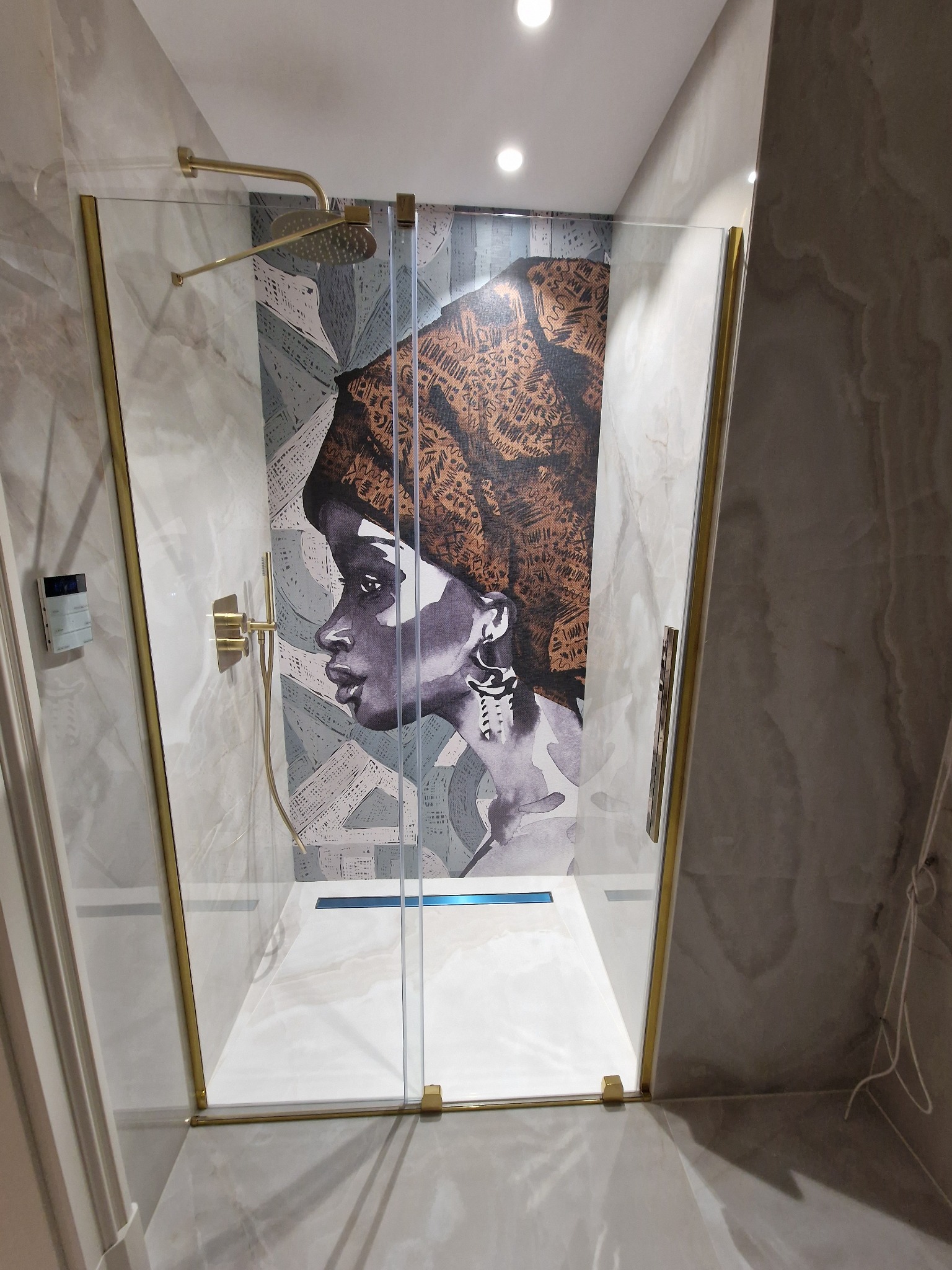 Kabina prysznicowa z grafiką kobiety w turbanie na szklanej ściance, złote wykończenia, marmurowe płytki na ścianach i podłodze.
