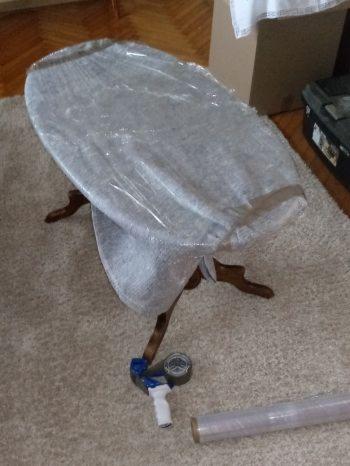 Owalny stolik z drewnianymi nogami owinięty folią stretch, przygotowany do transportu, obok leży dyspenser do folii.