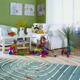 Instalacja ogrzewania podłogowego w pokoju dziecięcym, widoczne rury grzewcze przed wylaniem wylewki, zabawki dziecięce w tle, zielona ściana z obrazami.