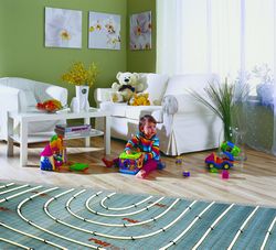 Instalacja ogrzewania podłogowego w pokoju dziecięcym, widoczne rury grzewcze przed wylaniem wylewki, zabawki dziecięce w tle, zielona ściana z obrazami.