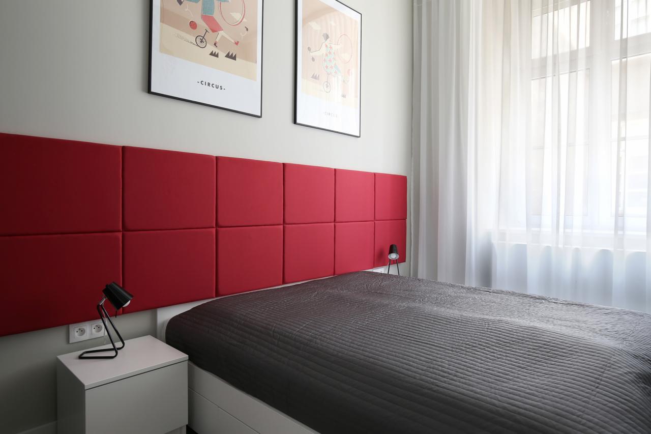 Nowoczesna sypialnia w Liszkach z czerwonym panelem tapicerowanym za łóżkiem i plakatami z motywem cyrkowym na ścianie.