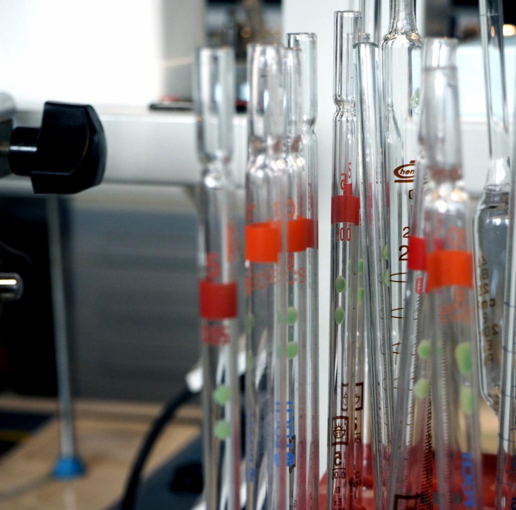 Szklane probówki z czerwonymi i zielonymi oznaczeniami, ustawione w stojaku laboratoryjnym, widoczne w laboratorium.