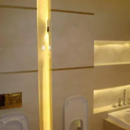 Beżowa łazienka z podświetleniem LED wzdłuż ścian, dekoracyjna tapeta z motywem roślinnym, zabudowa toalety i wanna z armaturą