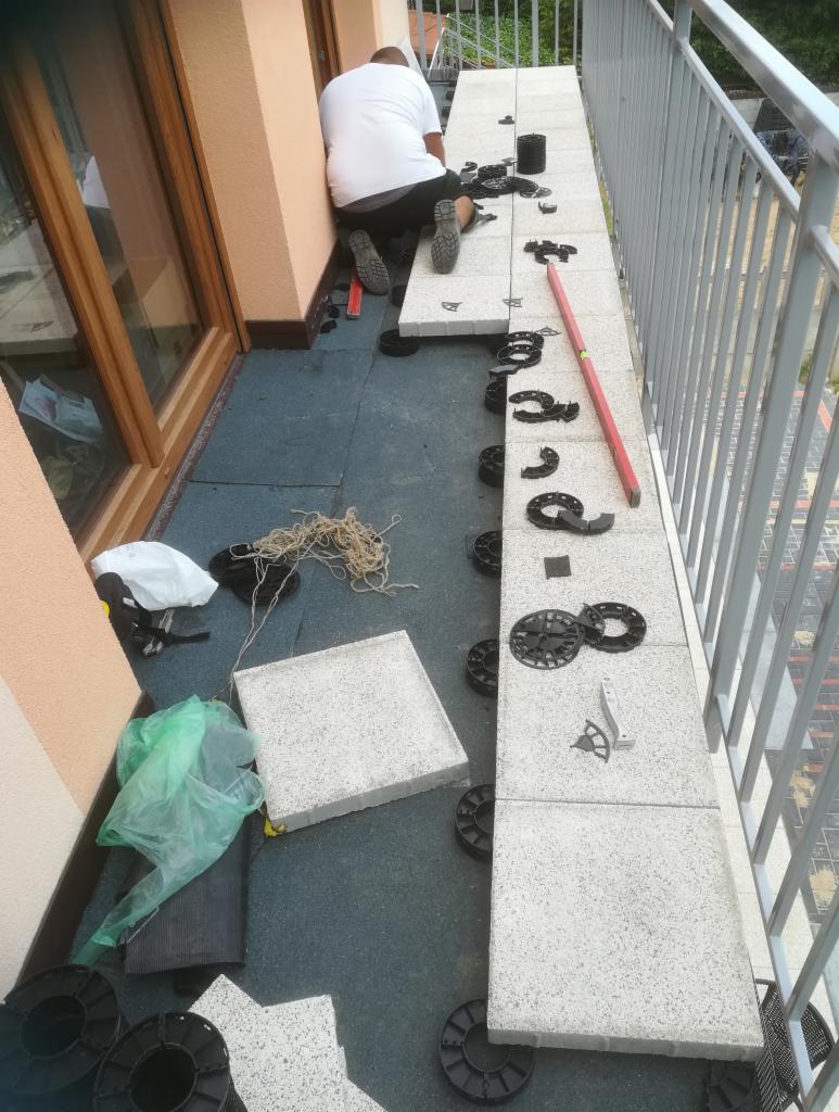 Montaż podestu z płyt betonowych na regulowanych wspornikach na balkonie, widoczne narzędzia i poziomica.