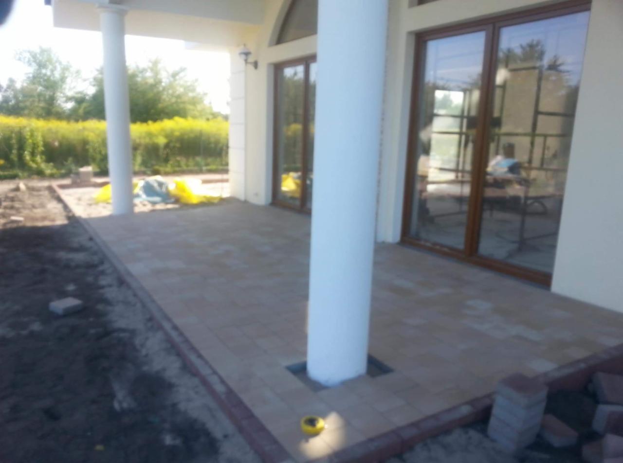 Beżowa kostka brukowa na tarasie z kolumnami, widoczne niedokończone obrzeża i resztki kostki.