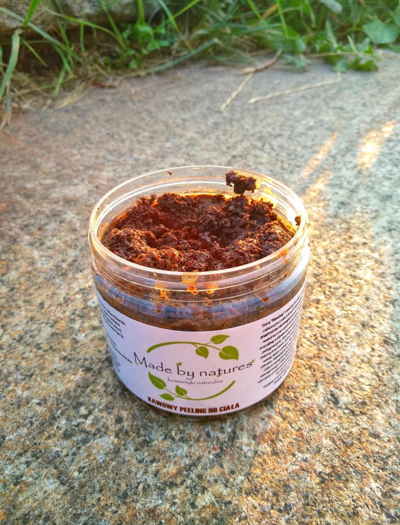 Otwarty słoik z kawowym peelingiem do ciała 'Made by natures' na szorstkiej, kamiennej powierzchni w promieniach słońca.