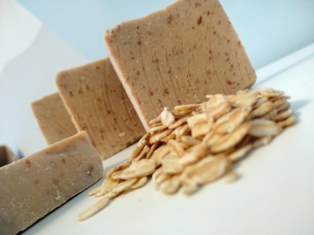 Cztery kostki beżowego mydła z płatkami owsianymi na białym tle, z wyraźnie widoczną teksturą i dodatkiem płatków owsianych.