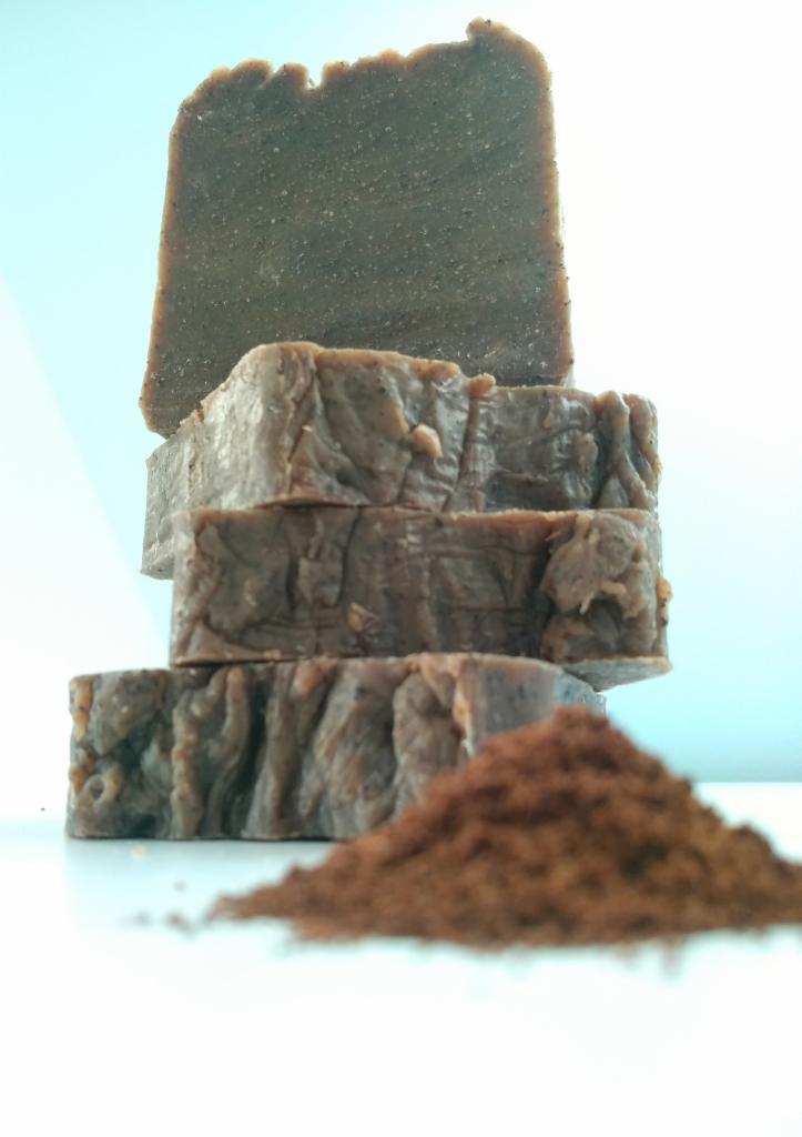 Ułożone w stos brązowe kostki mydła o nieregularnej fakturze, obok nich kopczyk brązowego proszku na białym tle.