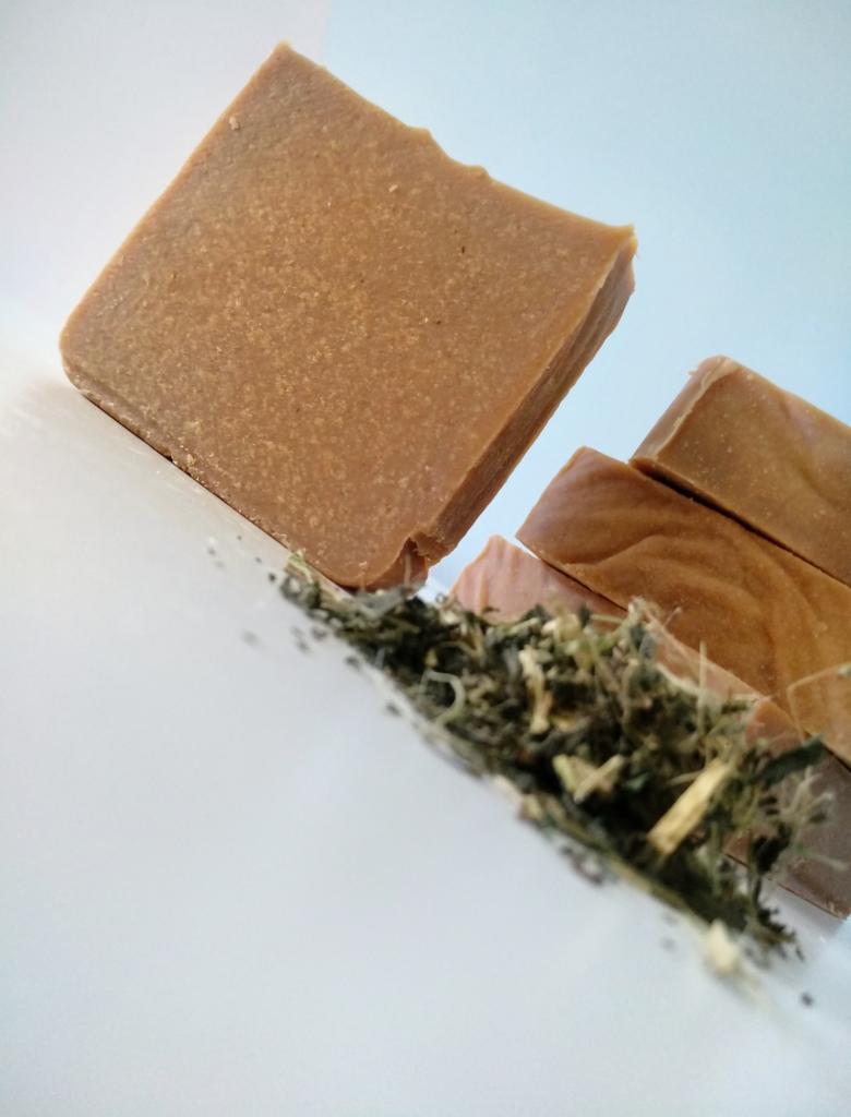 Trzy kostki brązowego mydła rzemieślniczego z zatopionymi ziołami na białym tle, ułożone pod kątem.