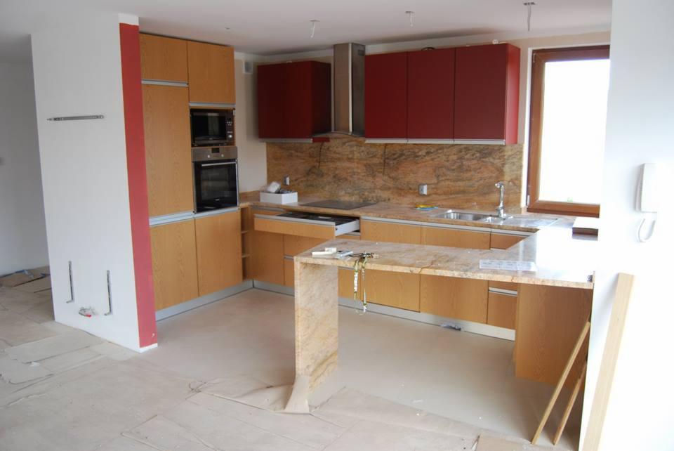 Montaż kuchni na wymiar: widok na częściowo ukończoną zabudowę z blatem z kamienia, czerwone szafki wiszące i zabezpieczoną podłogę.