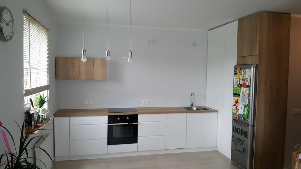 Minimalistyczna kuchnia: białe szafki z drewnianym blatem, wisząca szafka z forniru i srebrna lodówka ozdobiona rysunkami dziecięcymi.