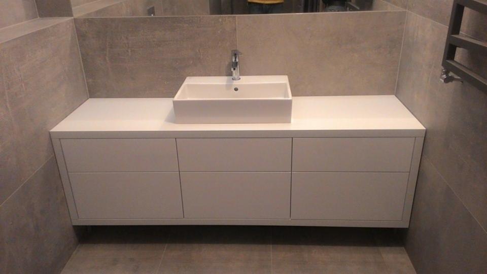 Nowoczesna łazienka z podwieszaną białą szafką z szufladami pod umywalką w kształcie prostokąta, bateria chromowana, szare płytki na ścianach i podłodze, grzejnik drabinkowy po prawej stronie.