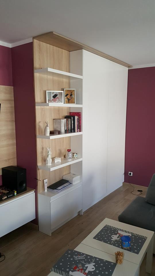 Biała szafa wnękowa z otwartymi półkami z jasnego drewna, dopasowana do wysokości pomieszczenia, z dekoracjami na półkach, na tle ściany w kolorze burgundu.