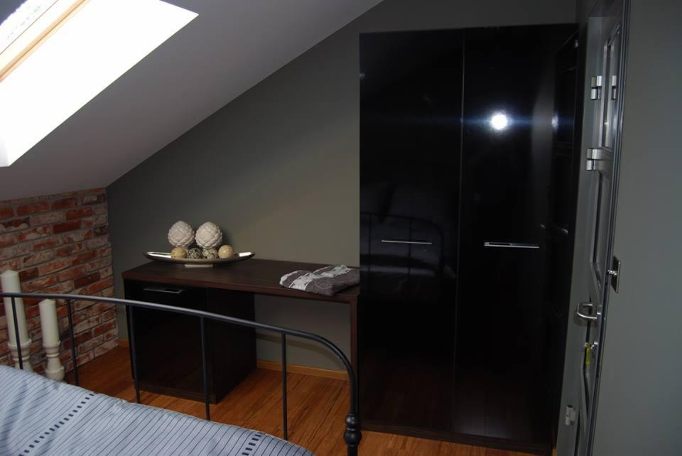 Czarne, lakierowane szafy przesuwne na poddaszu, obok biurka z dekoracjami, widok z perspektywy łóżka z metalową ramą.