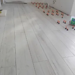 Układanie podłogi z płytek imitujących drewno, z użyciem systemu poziomowania płytek w pomieszczeniu w trakcie remontu.