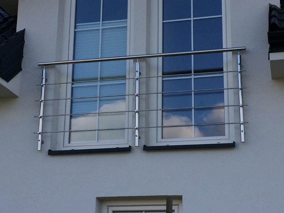Zewnętrzna, minimalistyczna balustrada ze stali nierdzewnej, zamontowana przed oknami na elewacji budynku, z widocznym odbiciem chmur w szybach.