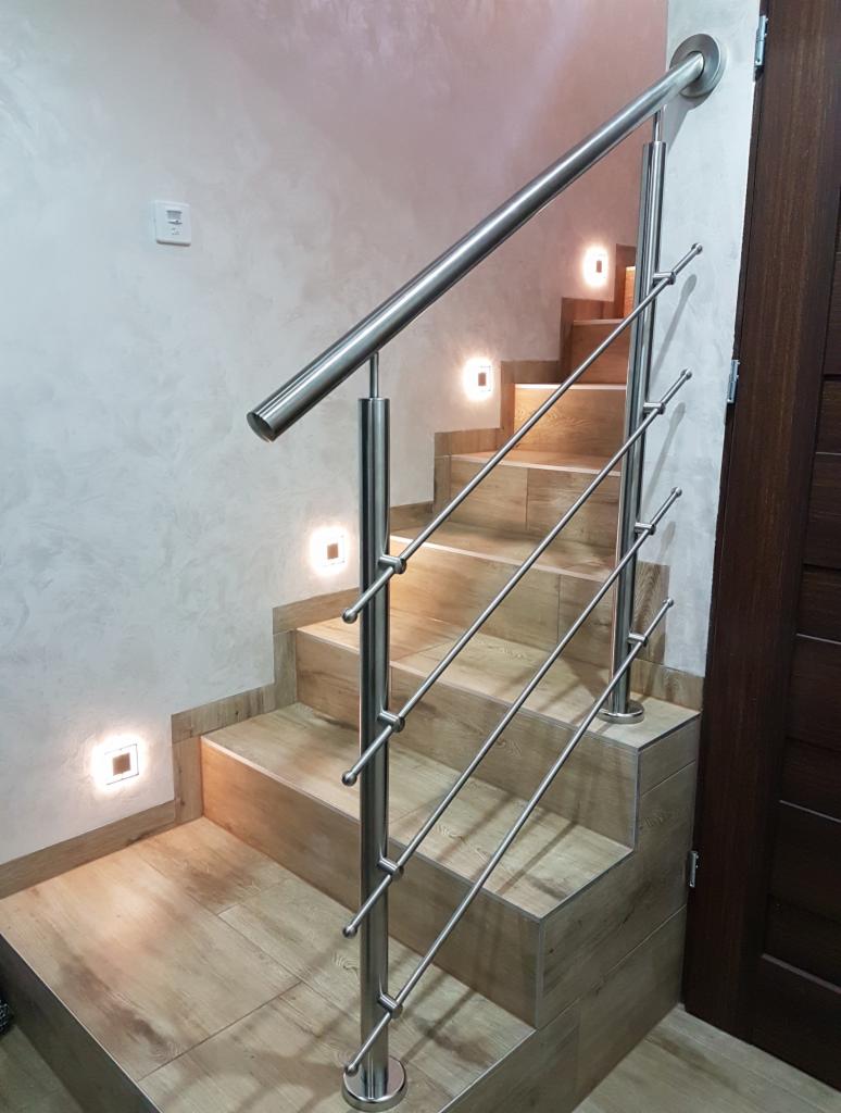 Nowoczesne schody z drewnopodobnych płytek z oświetleniem LED w stopniach i balustradą ze stali nierdzewnej z okrągłymi zakończeniami prętów.