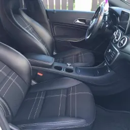 Wnętrze samochodu z czarną tapicerką w kratę, widoczne przednie fotele, deska rozdzielcza i kierownica.