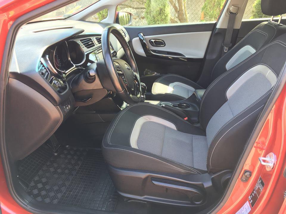 Wnętrze czerwonego samochodu marki Kia z czarno-szarą tapicerką foteli, widok z otwartych drzwi kierowcy.