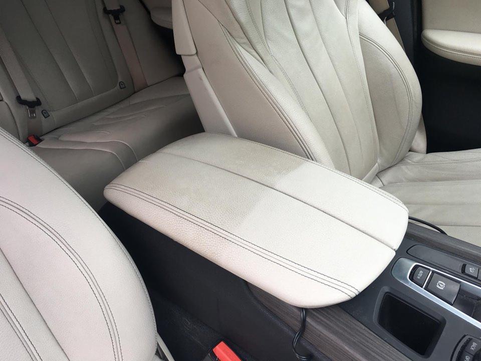 Jasna, skórzana tapicerka samochodowa z widoczną różnicą w czystości na podłokietniku po częściowym czyszczeniu.