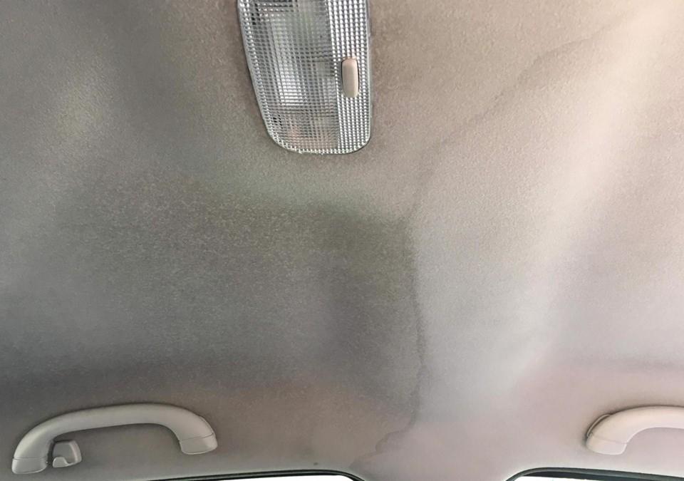 Wnętrze samochodu z widocznym, częściowo wyczyszczonym sufitem tapicerowanym, z wyraźnym kontrastem między obszarem wyczyszczonym a zabrudzonym, oświetlonym przez wewnętrzną lampkę.