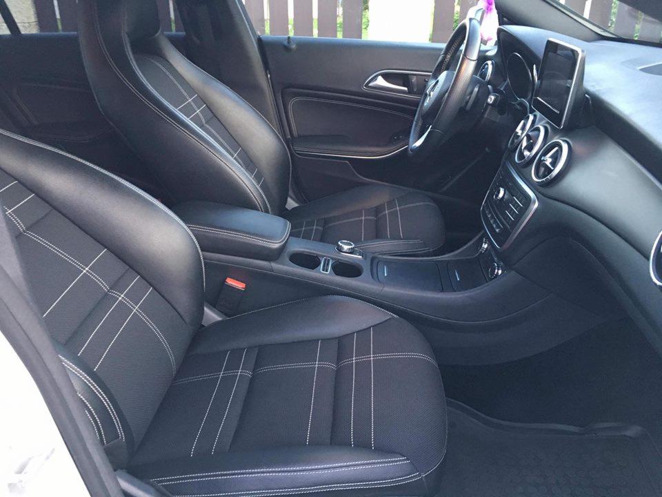 Wnętrze samochodu z czarną tapicerką w kratę, widoczne przednie fotele, deska rozdzielcza i kierownica.