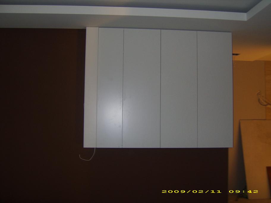 Pionowe, białe szafki wiszące na brązowej ścianie, widoczne kable wystające spod szafki, ujęcie z dołu.