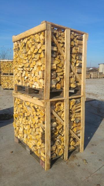 Drewno kominkowe pocięte na szczapy ułożone w drewnianej skrzyni na palecie, na placu składowania opału, w tle inne skrzynie z drewnem.