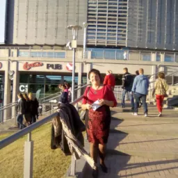 Kobieta w czerwonej bluzce stojąca na schodach przed budynkiem z napisem PUB w Miszewku, w tle przechodzący ludzie.