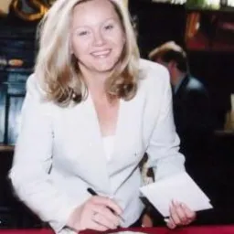 Kobieta w białym żakiecie podpisuje dokument na stole w Gliwicach, w tle widoczny mężczyzna.