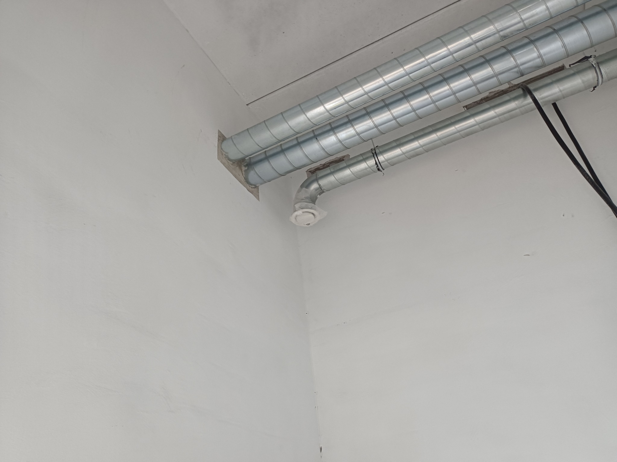 Szare, spiralne rury wentylacyjne przytwierdzone do sufitu i ściany. Widoczny biały nawiewnik. Ujęcie z dołu, podkreślające instalację w rogu pomieszczenia.
