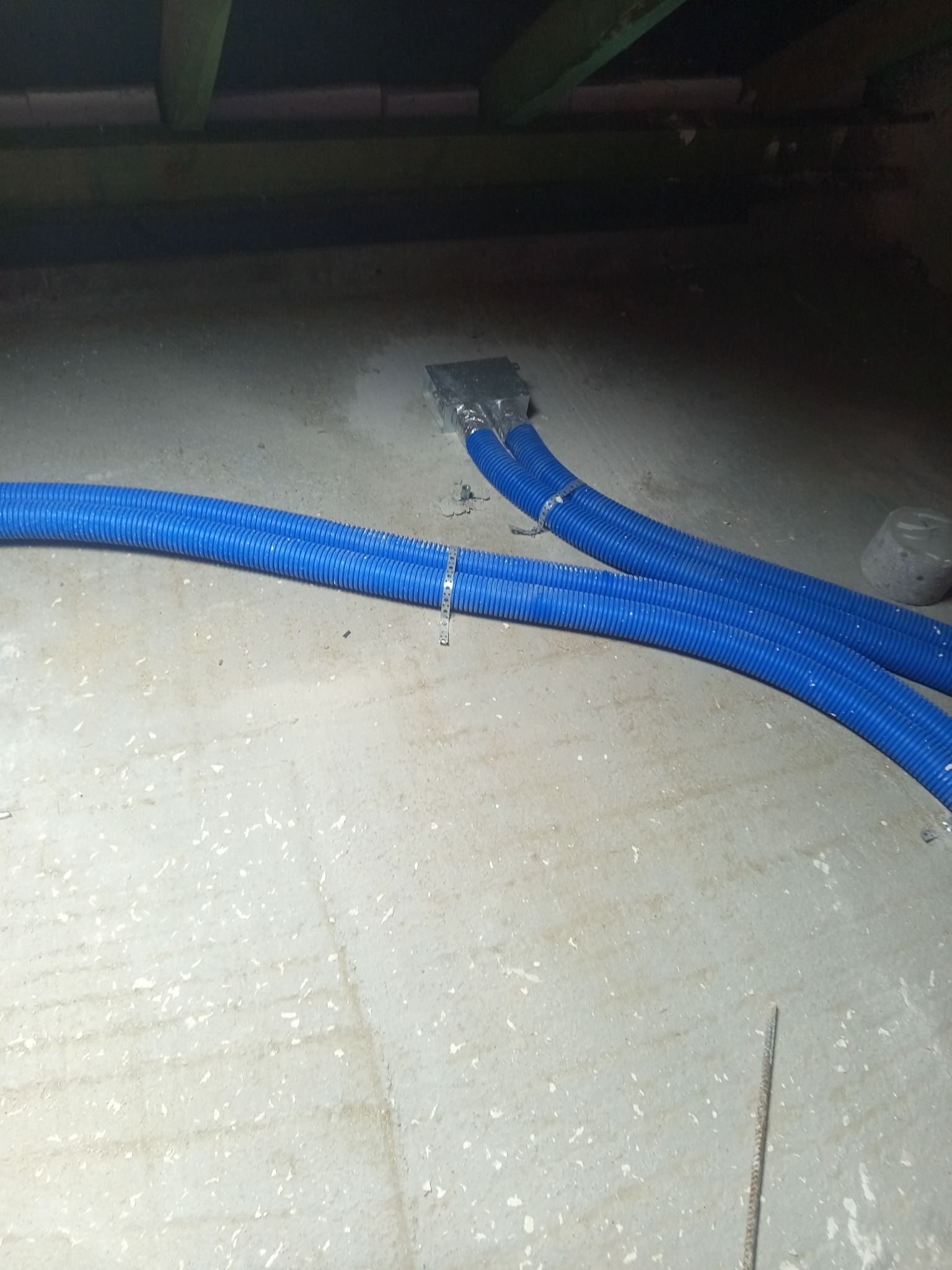 Niebieskie, elastyczne przewody wentylacyjne przymocowane do metalowej puszki na szarej, betonowej podłodze w słabo oświetlonym pomieszczeniu.