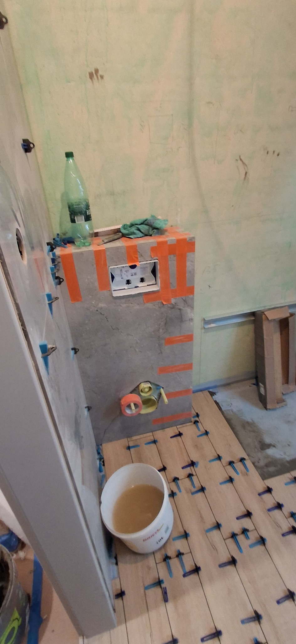 Łazienka w trakcie prac: częściowo ułożona podłoga z płytek drewnopodobnych z użyciem klipsów poziomujących, widoczna instalacja podtynkowa i ściana z przygotowanymi płytkami.