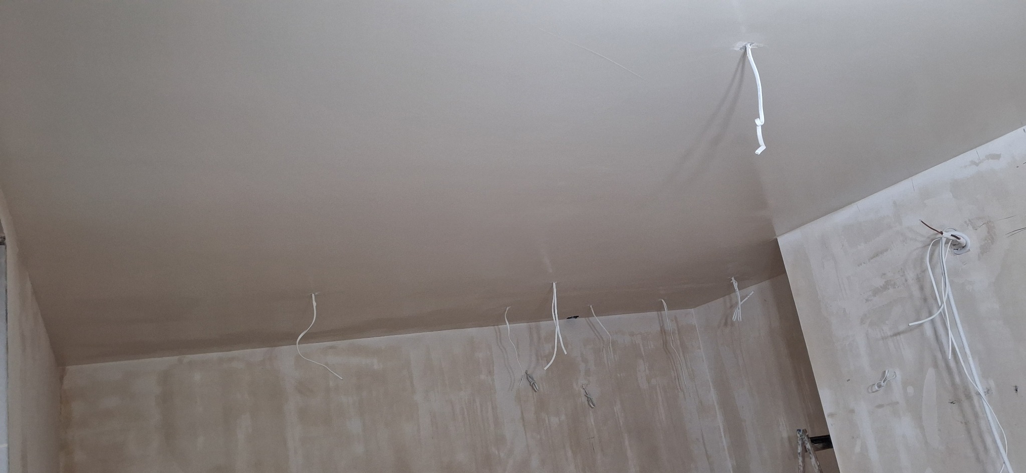 Wnętrze w trakcie prac wykończeniowych: gładki sufit po szpachlowaniu, wystające przewody elektryczne, ściany przygotowane do malowania. Widok z dołu, ukośne ujęcie.