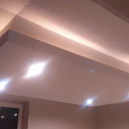 Podwieszany sufit z oświetleniem LED, widoczne okno w tle, ciepłe światło.