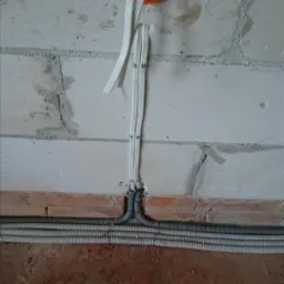 Wyprowadzone przewody elektryczne ze ściany z cegły i betonu, zabezpieczone peszlami przy podłodze.