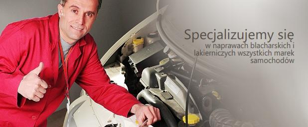 Uśmiechnięty mechanik w czerwonym kombinezonie pokazuje kciuk w górę, stojąc przy otwartym silniku samochodu. Na silniku widoczne żółte korki i czarne przewody. Częściowo zasłonięty napis reklamowy...