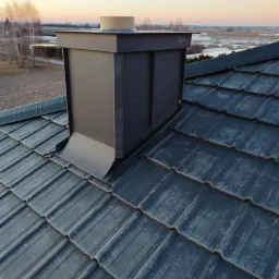 Nowy, grafitowy komin wentylacyjny na dachu z blachodachówki, widok z góry na tle krajobrazu o zmierzchu.