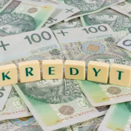 Stos banknotów 100 zł z ułożonym napisem 'KREDYT' z beżowych kostek z zielonymi literami.